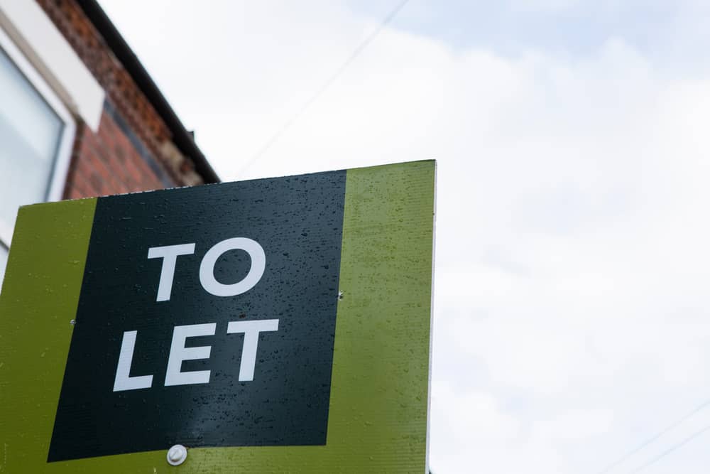 UK To Let sign with space to right of image. England housing market buy to let lettings sign in front of a red brick terrace house rental property with some sky 
