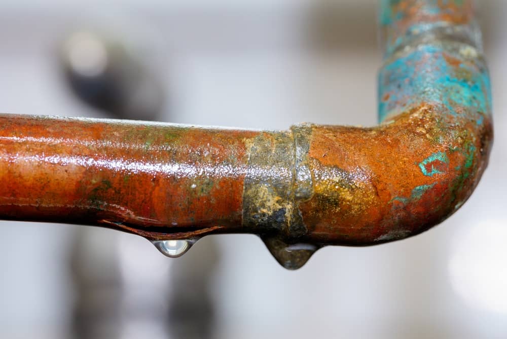 Leaking copper pipe with freeze damage representing burst plumbing, water damage, emergency repair, and home maintenance.