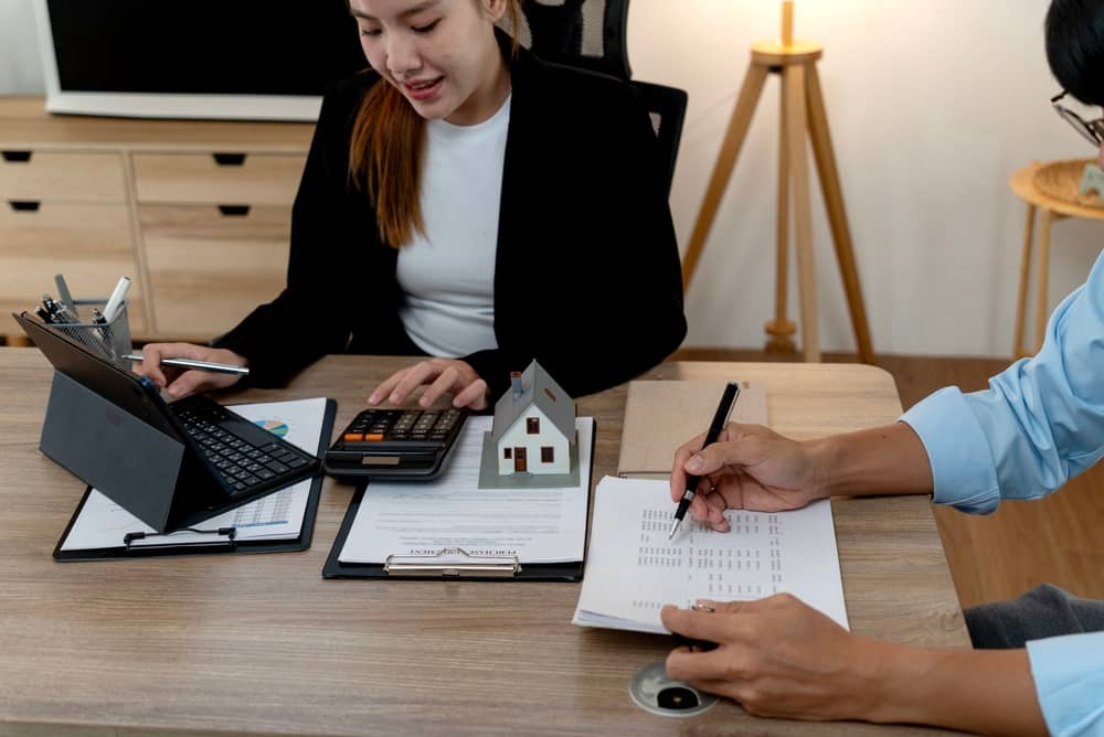 Real estate consultant using calculator to discuss housing finance with client. Ideal for mortgage, property investment, loan agreement, and financial planning content.